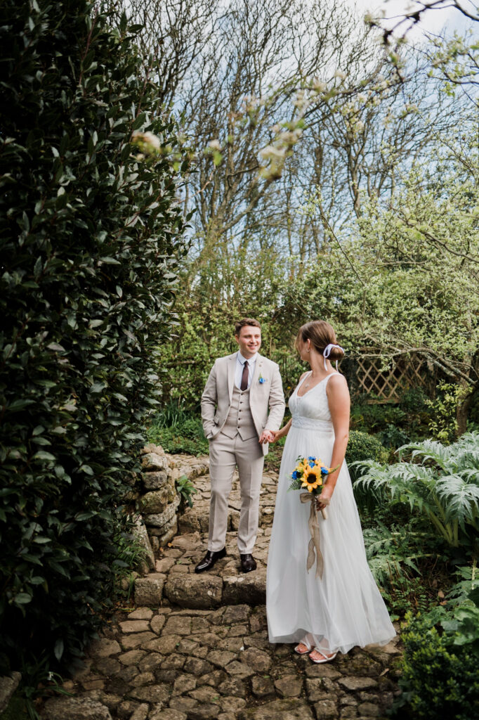 A newlywed couple walking through the gardens looking at each other at Pengersick Castle in Cornwall