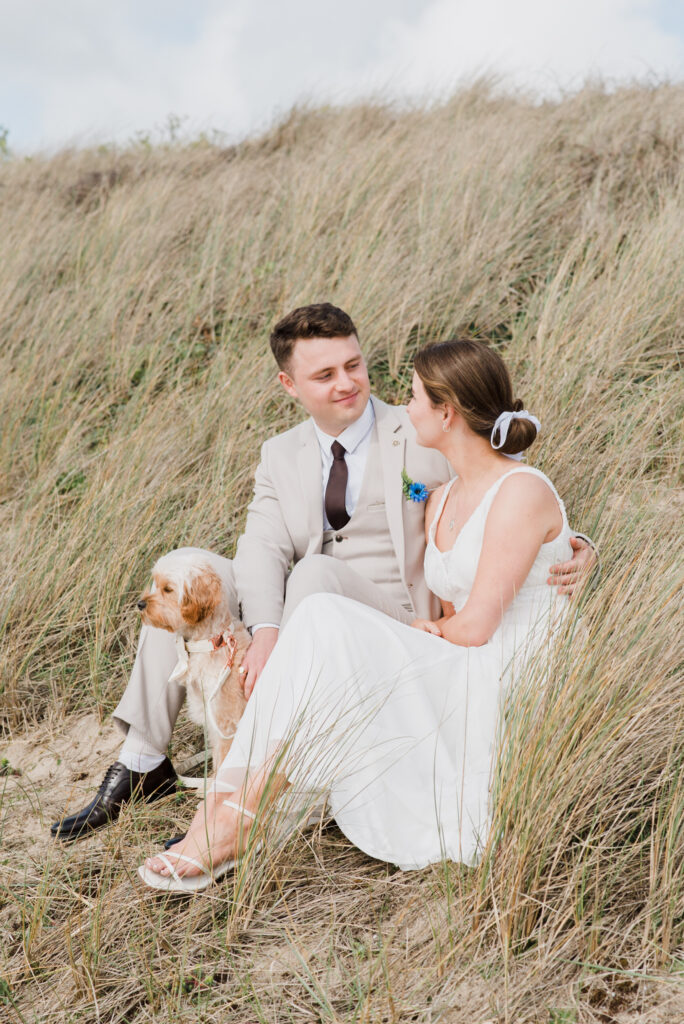 A newlywed couple sitting on a grassy bank at Praa Sands in Cornwall
