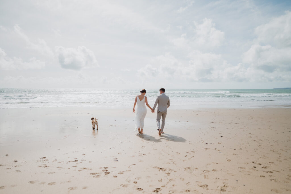 A newlywed couple walking towards the sea at Praa Sands in Cornwall