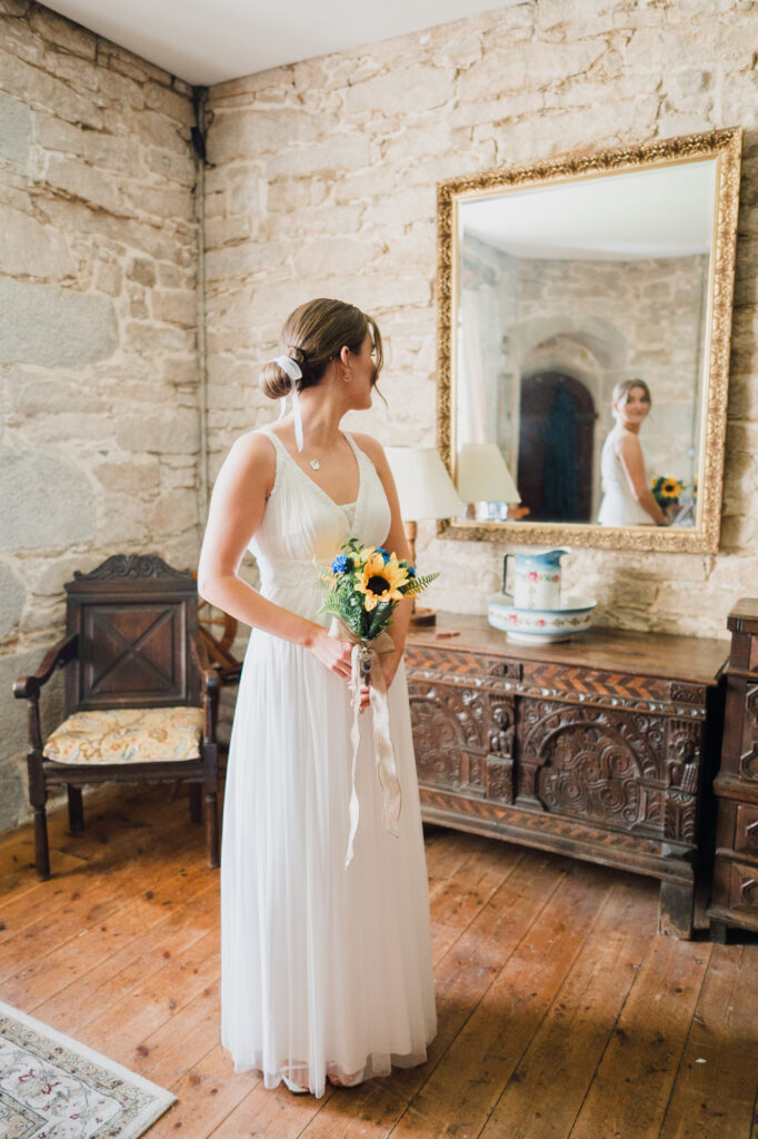 A bride in her wedding dress looking at a mirror inside Pengersick Castle in Cornwall